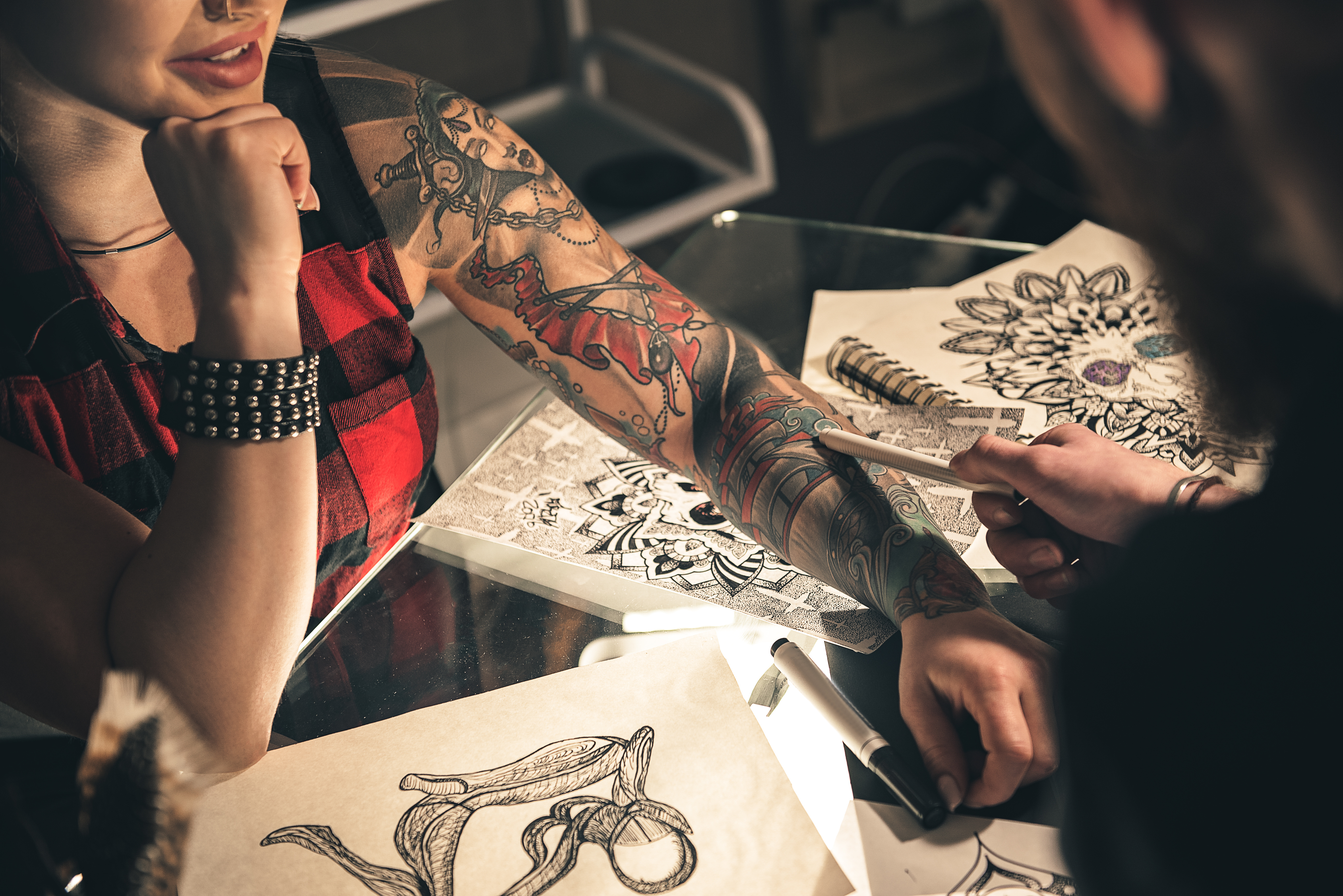 woman with tattoos sitting at a table with man showing design sheets