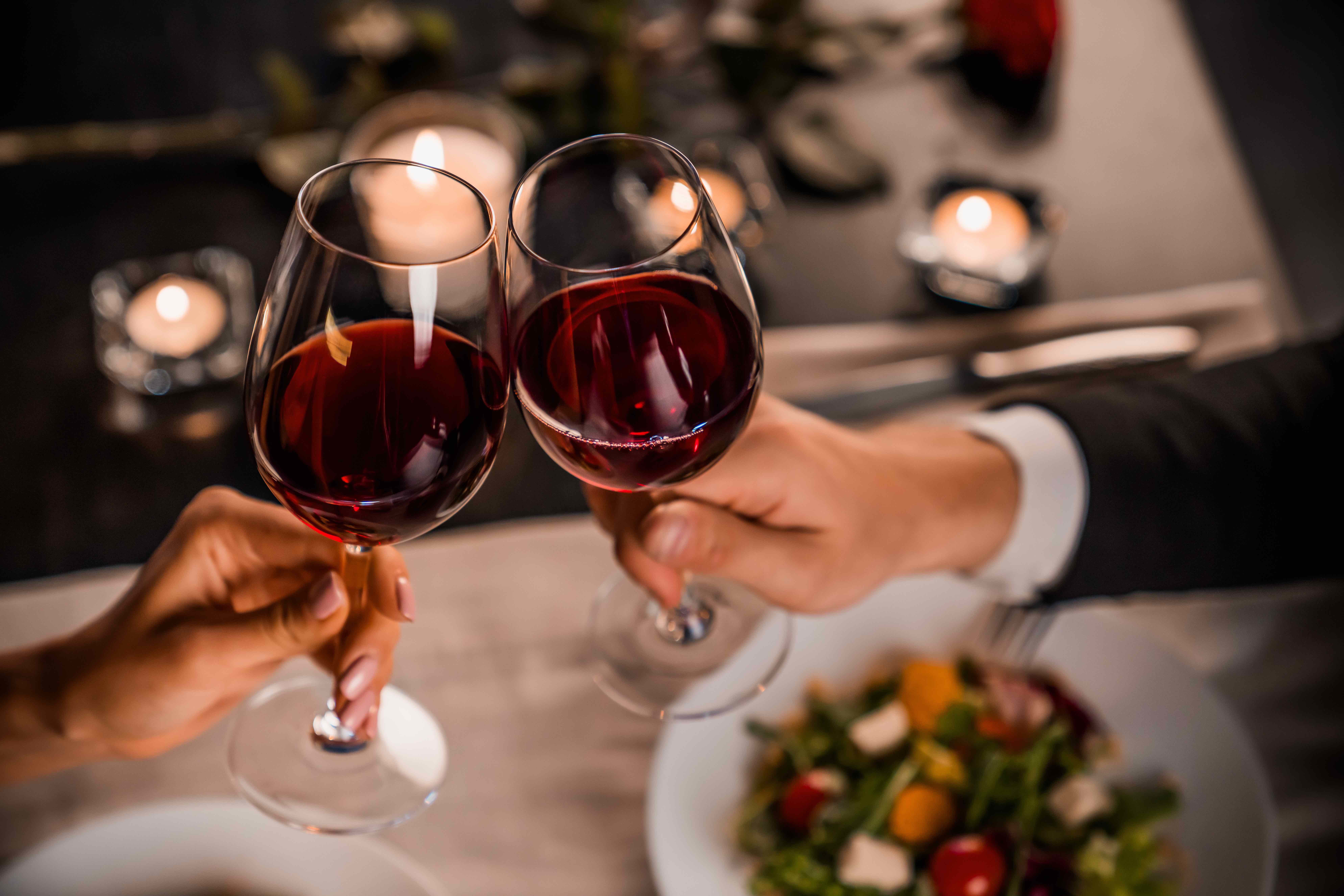 two hands holding glasses with red wine over a table