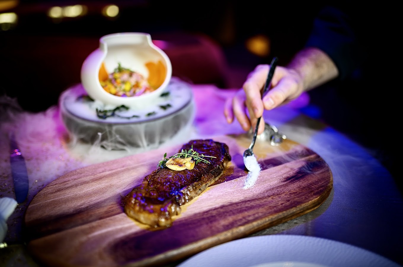 steak on a wooden plate with ceviche in a white bowl behind