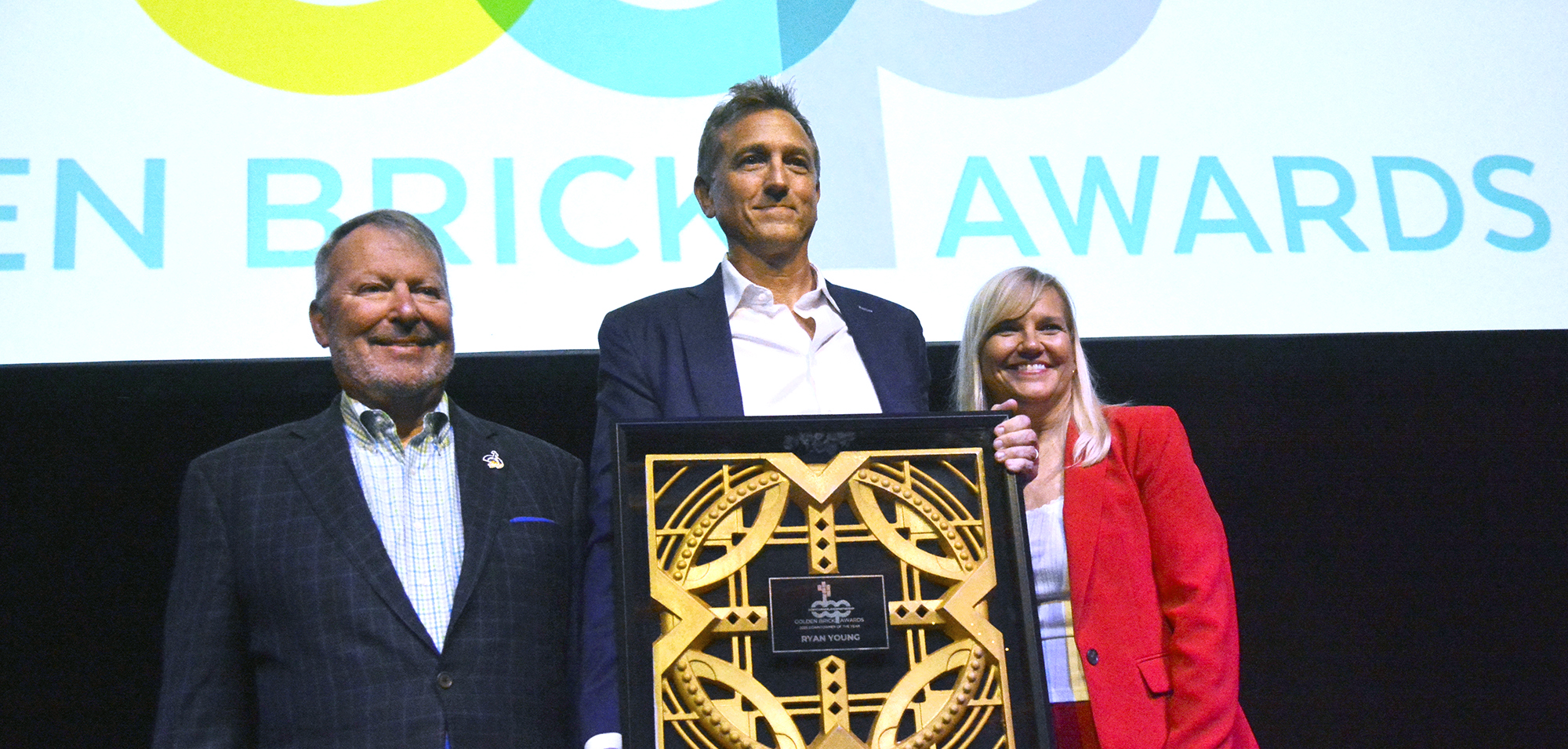 Mayor Buddy Dyer, Ryan Young and Jill Vaughn stand onstage with the Downtowner of the Year Award.