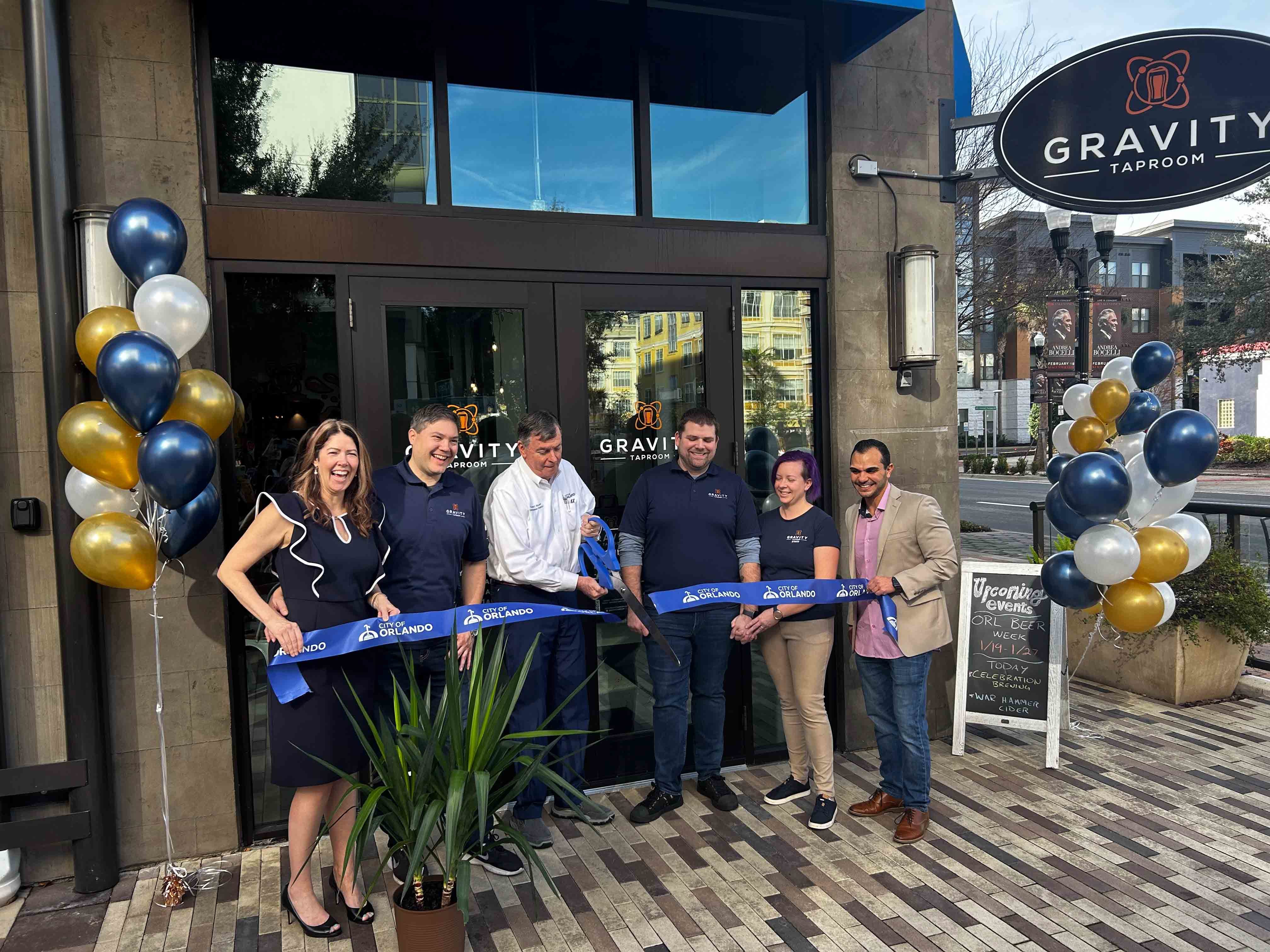 six people in front of a restaurant with grand opening ribbon