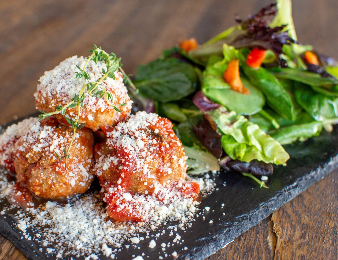 meatballs with parmesan and side salad on a black plate