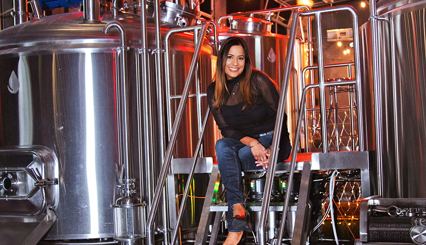 A woman sitting on metal steps between two large aluminum tanks, wearing a black shirt and jeans