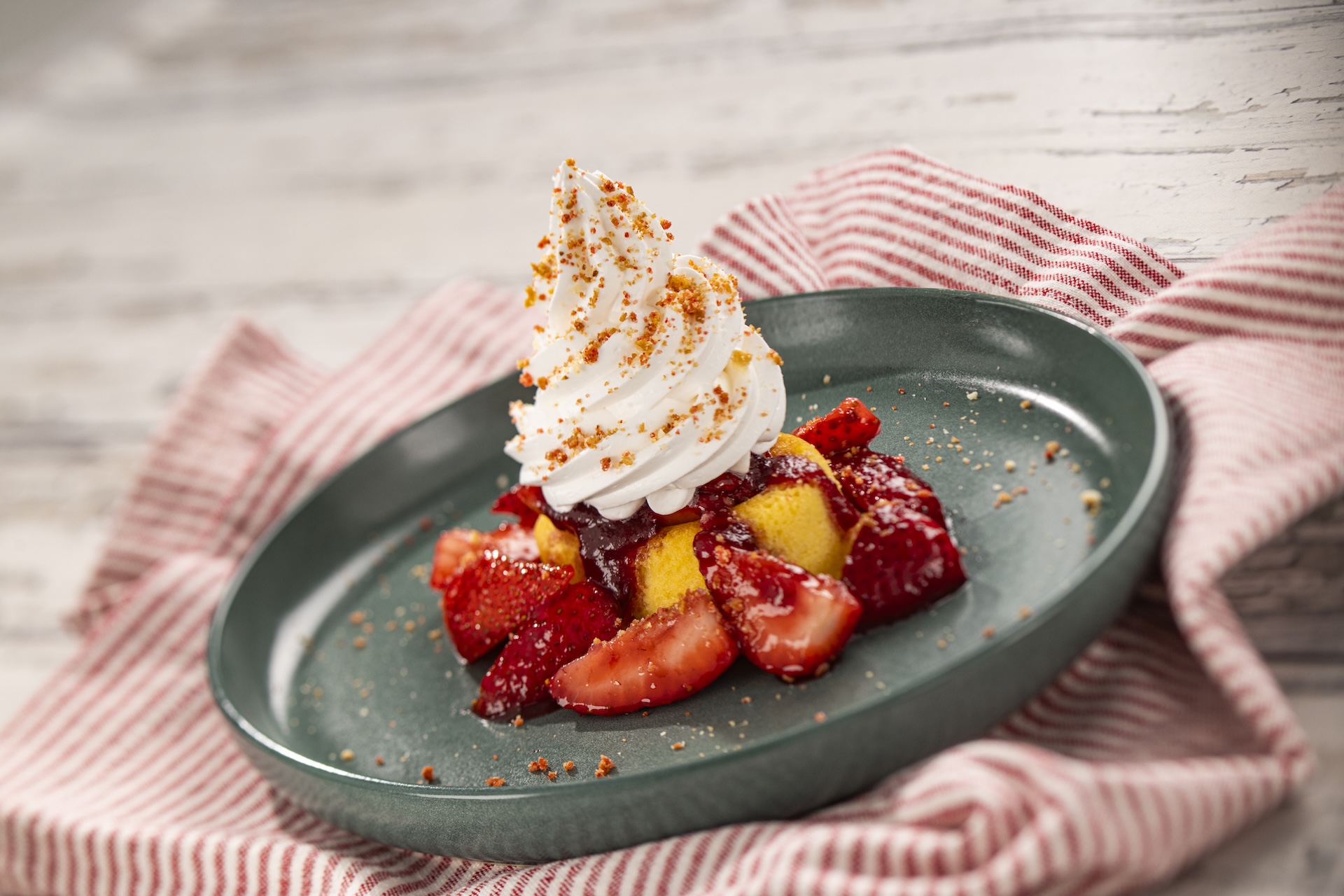 A strawberry shortcake on a white plate with a red and white striped napkin