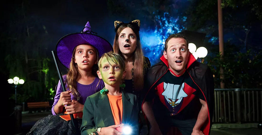 four kids in halloween costumes looking above camera and scared